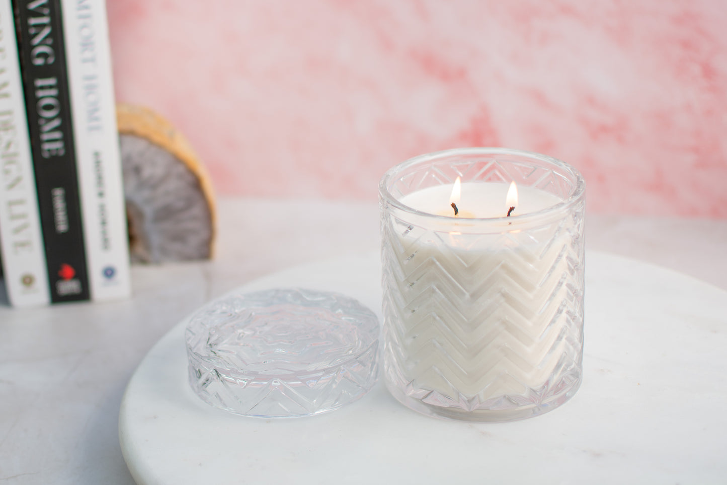 Chevron embossed lit unscented candle on marble surface with home books in background