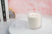 Chevron embossed lit unscented candle on marble surface with home books in background