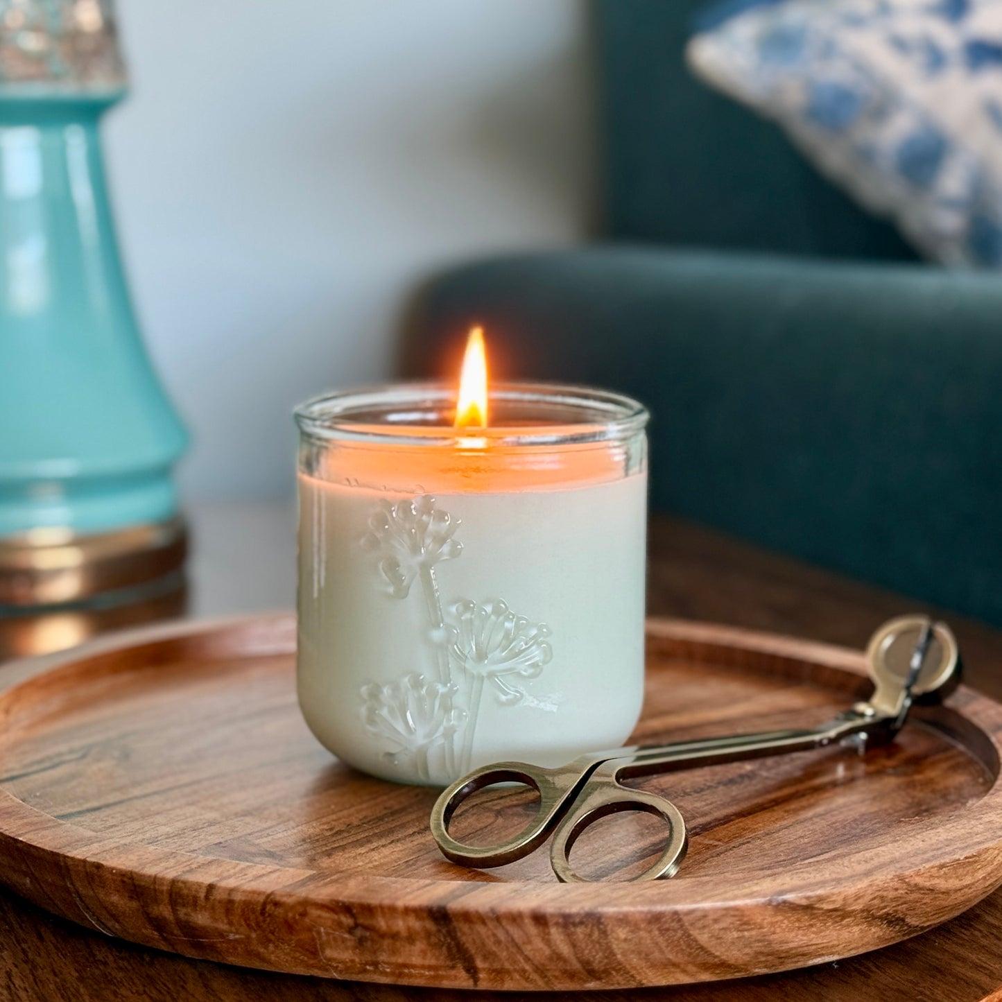 A lit, fragrance free candle with wick trimmer on side table by Unscented Candle Company