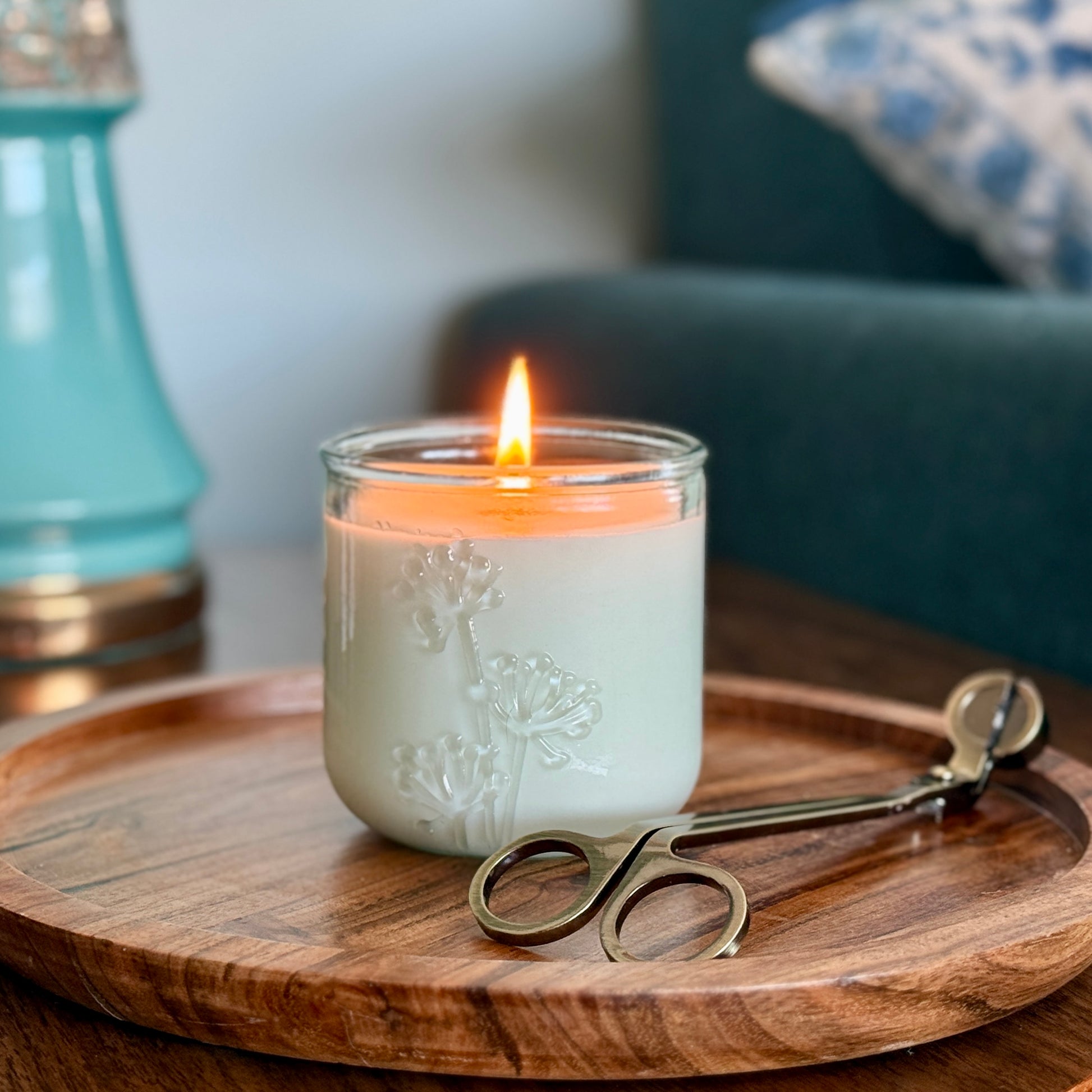 A lit, fragrance free candle with wick trimmer on side table by Unscented Candle Company