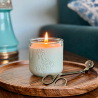 A lit, fragrance free candle with wick trimmer on side table by Unscented Candle Company