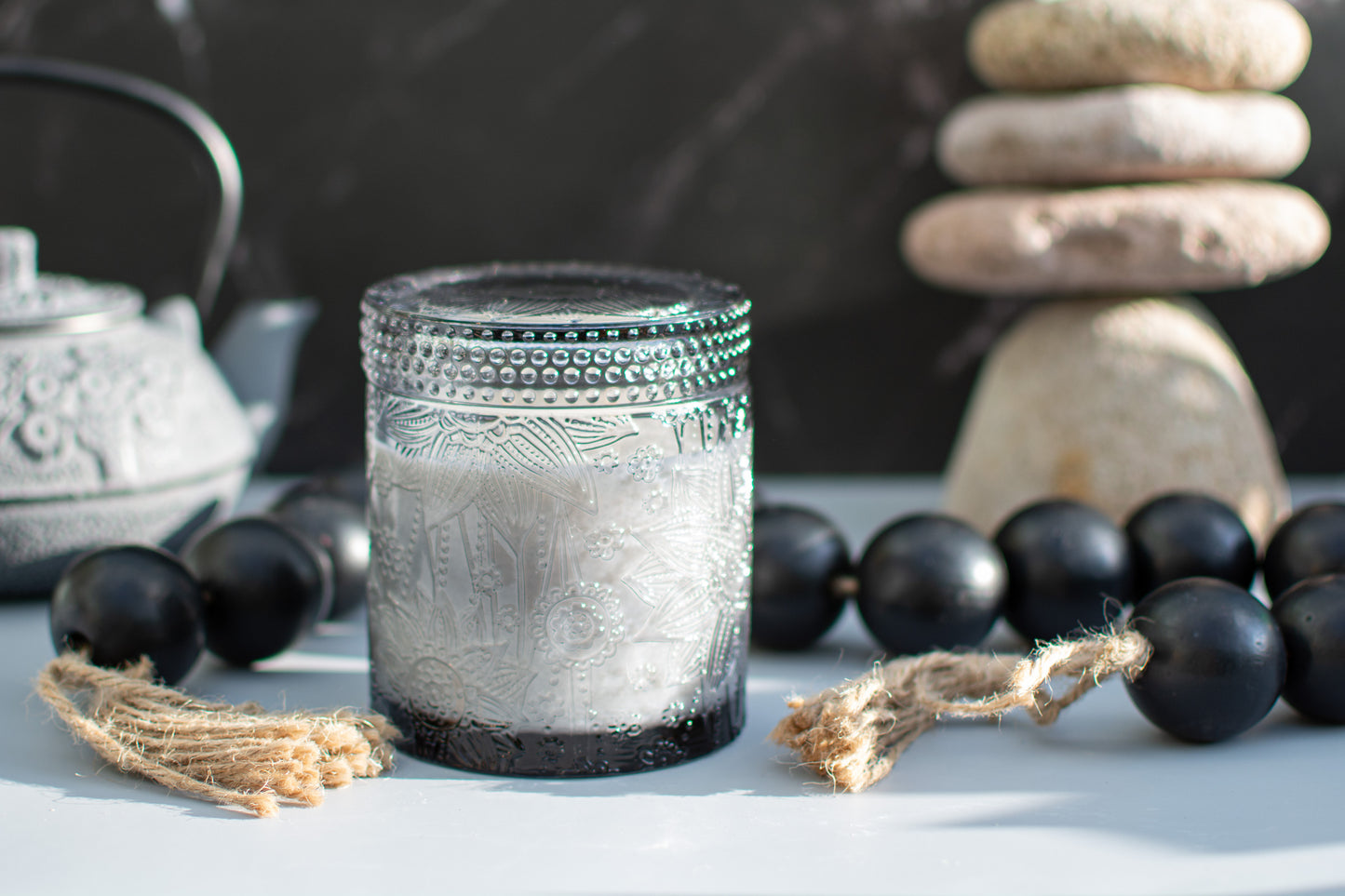 Lotus embossed unscented candle, surrounded by black beads and a teapot